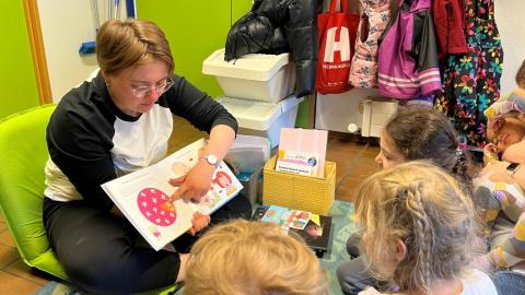 Photo of a preschool staff member showing pictures in a book to children.