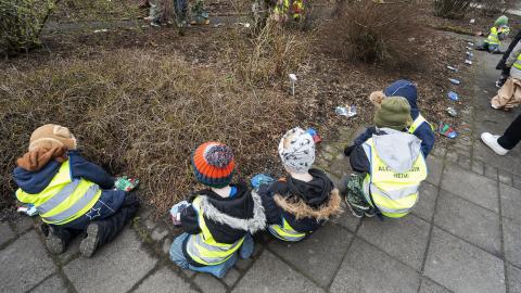 Preschool children seen from behind crouching by a garden bed. 