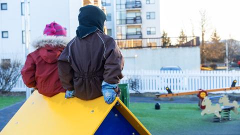 Börn sitja upp á litlum kofa á leikskólalóð.