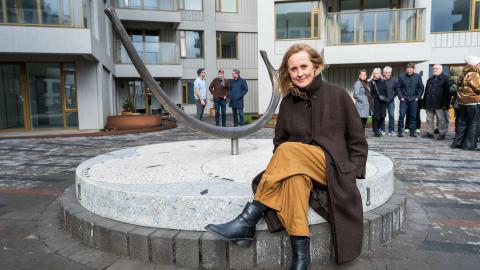 Anna Júlía Friðbjörnsdóttir við verk sitt Rif í Vesturvin. Situr á verkinu, fólk í baksýn sem var við vígslu á verkinu.