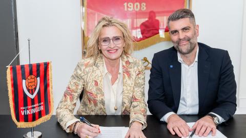 Heiða Björg Hilmisdóttir borgarstjóri og Björn Einarsson formaður Víkings sitja við borð að undirrita samning. Víkingsfáni á borðinu og á vegg á bakvið þau.